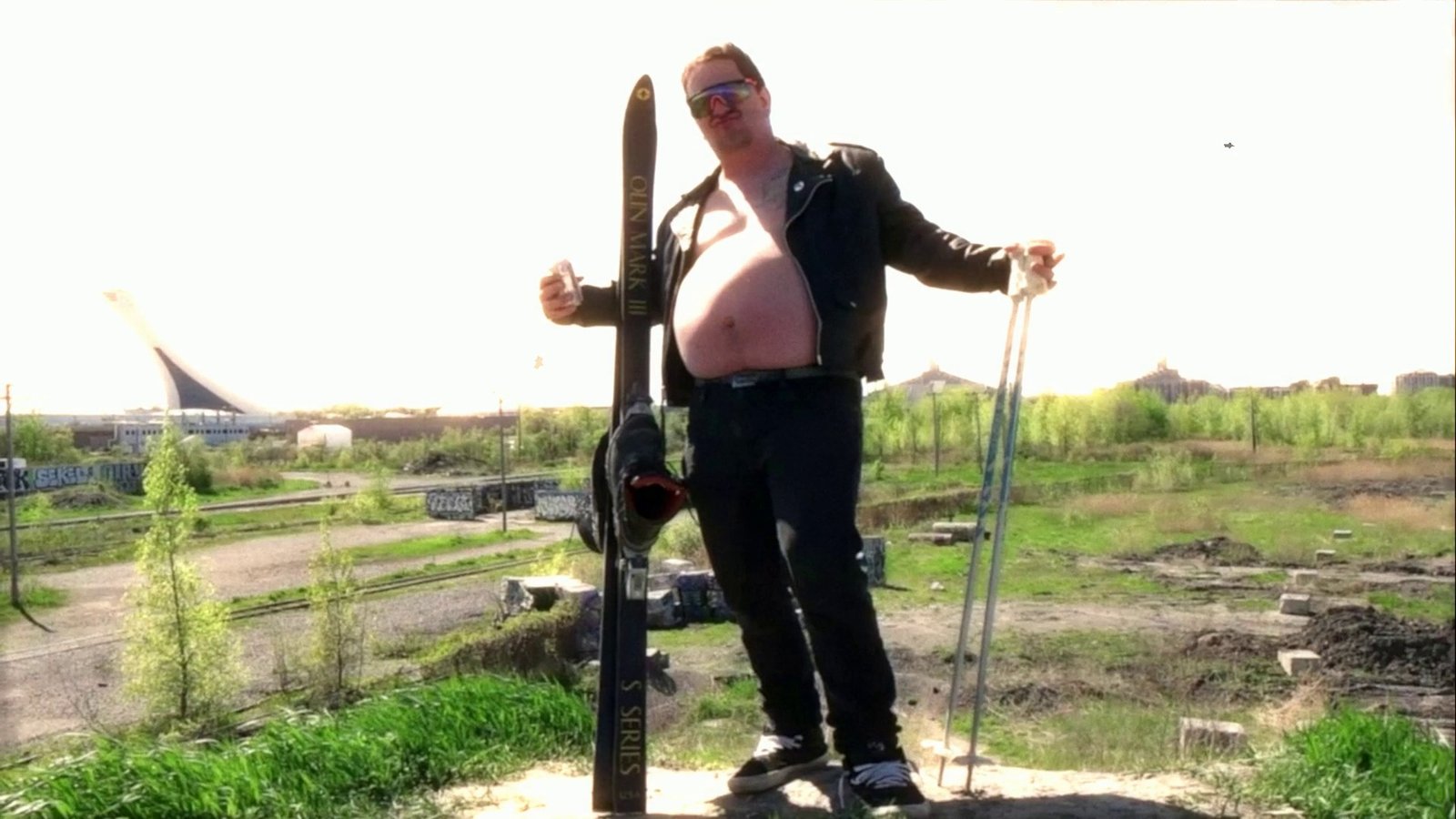 Daylight footage: a skier posing on a dirt lot with a stadium behind. After Super8 Film Lab, grindhouse (v2 engine) look: the retained V2 grindhouse engine.